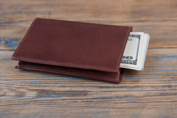 Brown leather wallet with one hundred dollar bills on wooden table. Top view