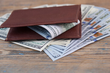 Brown leather wallet with one hundred dollar bills on wooden table. Top view