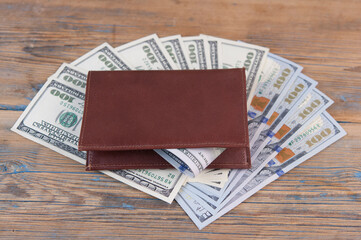 Brown leather wallet with one hundred dollar bills on wooden table. Top view