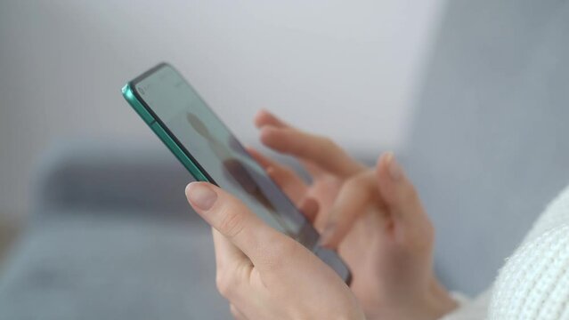 Close-up of beautiful female hands with a modern smartphone. The girl is viewing the content of the online store. Side view, the screen is blurry.