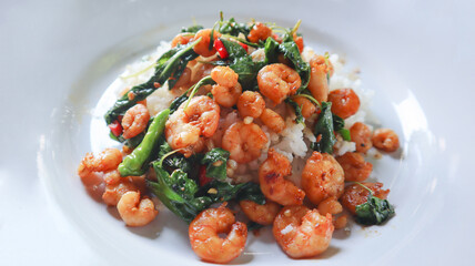 Traditional fried spicy peeled shrimp with chilly and basil on white plate. Famous hot and spicy menu in Asia. Luxury stirred prawn with herbal vegetable. Thailand call Pad Kaprao. Thai local food