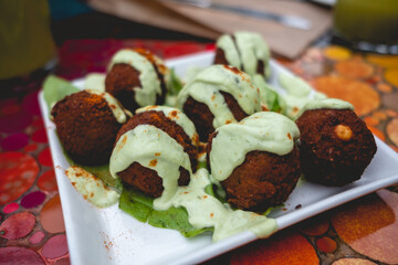 Closeup of white plate with gourmet 'falafel' (mixture of ground spiced chickpeas shaped into balls and deep-fried), with sauce and merken (smoked chili pepper) in a table in the day