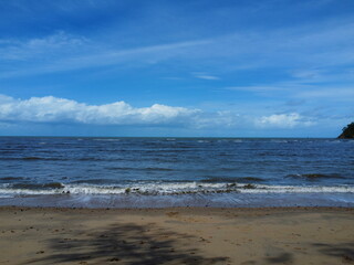 Fototapeta na wymiar View of waves crashing onto beach with blue sky