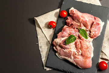 Raw turkey thigh with spices. Fresh boneless meat on a ceramic stand. Hard light, dark shadow