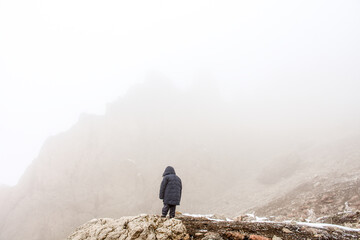 kid stands peak of rock and other rocky hill hardly seems in fog