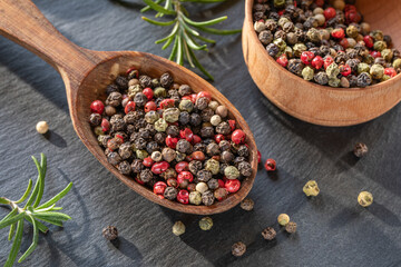 Peppercorns seeds of different colors in wooden spoon closeup, black background