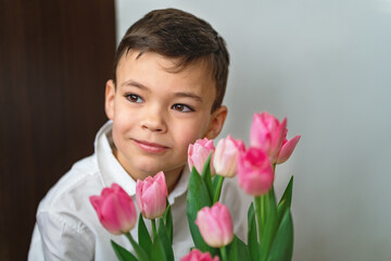 Portrait of a cute smiling young Caucasian boy with a beautiful bouquet of pink tulips on the foreground. Mother's Day concept.