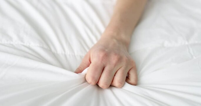 Woman hand clutches blanket on bed in pain