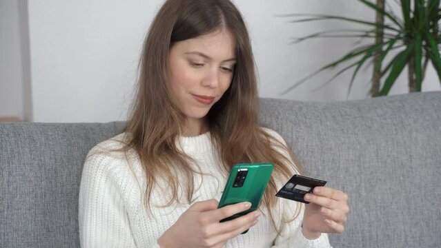 A young girl sits with a phone in one hand and a bank card in the other. Online shopping concept. Side view.