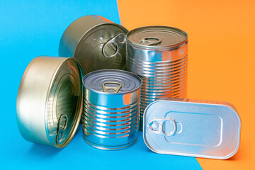 A Group of Stacked Tin Cans with Blank Edges on Split Blue and Orange Background. Canned Food. Different Aluminum Cans for Safe and Long Term Storage of Food. Steel Sealed Food Storage Containers