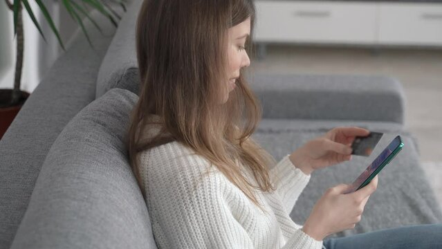 A young girl sits with a phone in one hand and a bank card in the other. Online shopping concept. Side view.