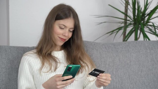 A young girl sits with a phone in one hand and a bank card in the other. Online shopping concept.
