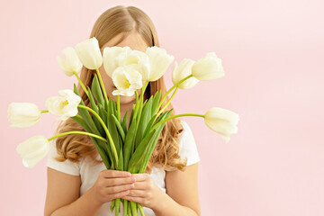 The concept of spring, happiness and holiday. Close-up portrait of a beautiful smiling girl holding a bouquet of white tulips in her hands eyes closed on a pink background