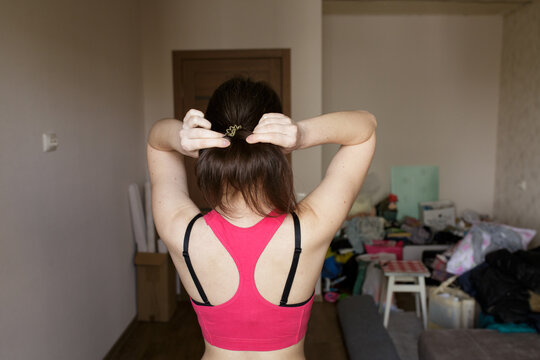 Beautiful Sports Girl In A Pink Top View From The Back. Girl Straightens Her Hair. House Cleaning.