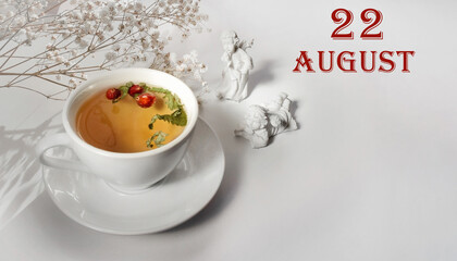 calendar date on light background with a porcelain cup of green tea, white gypsophila and angels with copy space. August 22 is the twenty-second day of the month