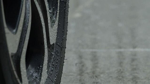 Rain splashing and car tire in rainwater. Car parking in the rain. Raining season and tires on the wet pavement. Close up of car tyre or wheels on a wet road. Represent auto in rainy season concept.