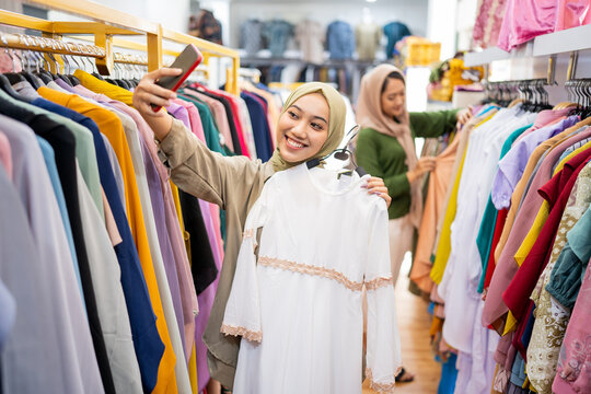 Beautiful excited muslim females with head scarf take picture of new dress thats she bought in fashion store