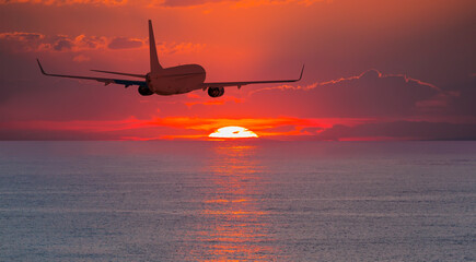 Airplane flying over tropical sea at sunset