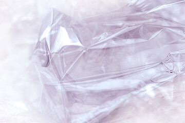 Obraz premium Texture of a plastic transparent cellophane package on a purple background. The plastic surface is wrinkled and torn, forming an abstract pattern.