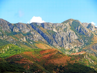 A wall of mountains rises above the valley. Warm tones on a sunny day with a small village in the hills. Mountains rock granite