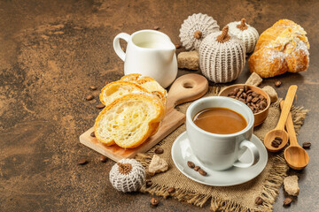 Breakfast concept with a cup of coffee, croissants, milk jug, and decorative crochet pumpkins