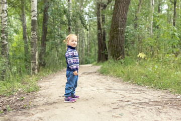 A little girl toddler is standing on a path in the spring forest. Nature walk