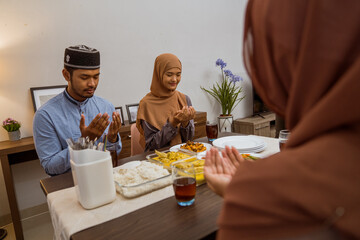 muslim people praying before break fasting iftar dinner together at home in ramadan celebration