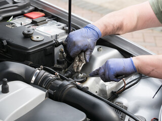 Pair of mechanic hands wearing blue gloves working in the engine bay of a sports car with plier...