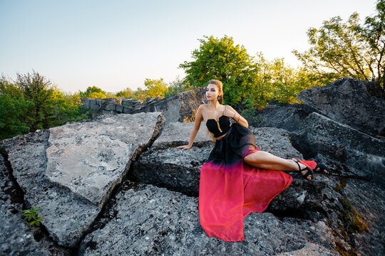 A girl in a summer dress lies on the rocks.