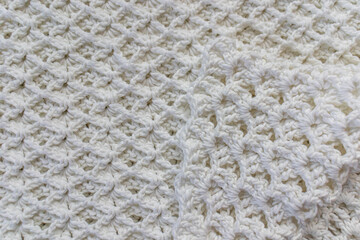 Close-up of a top view of a white cotton blanket with an original embossed crochet stitch pattern with a tip folded towards the center, handmade creativity