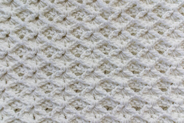 Close-up of a top view of a white cotton blanket with an original embossed crochet stitch pattern, handmade creativity