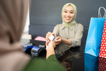 veiled worker woman smiles as she take credit cards from customer while paying cashless at the checkout counter at a boutique shop