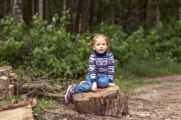 A little girl toddler is sitting on a stump in a spring park. Walk