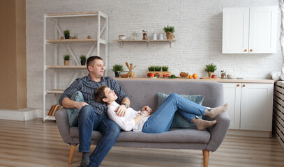 A happy dreamy young Caucasian couple is relaxing on the sofa in the designer living room. The girl is lying on the guy's lap.