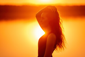 Fototapeta premium Close-up portrait of silhouette of curly, free girl, wind in her hair, light movements at sunset