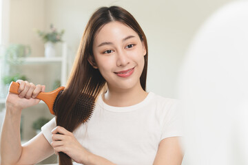 Happy asian woman brushing hair by wooden comb in the morning.