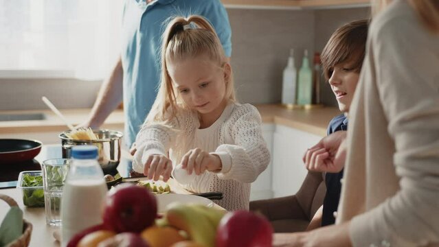 Close up of cute son and daughter learn how to cook omlet, having fun, helping parents in kitchen. Caucasian family with little kids prepare breakfast together at home.