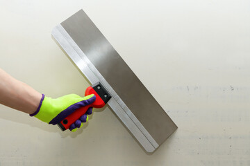 Clean Spatula in a male hand in a bright glove against a gray wall. Construction finishing works