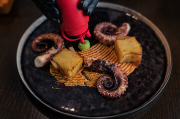 Chef preparing octopus with potatoes on pea mash decorated with edible flowers
