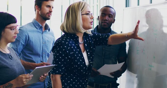 Bringing their ideas to life. 4K video footage of a diverse group colleagues brainstorming together on a whiteboard in a modern office.