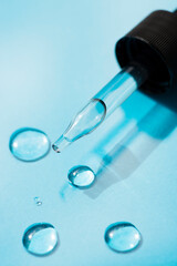 Open cap with close-up dropper pipette with drops of serum. Blue background with daylight and the appearance of the texture of the gel. Skin care products. Beauty concept for face and body care