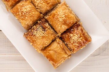 Classic sweet baklava with a white ceramic plate on a wooden table, macro, top view.
