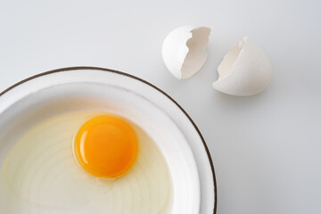 White egg broken egg with a yolk in a white plate. Cracked egg, eggshells with yolk on white background. Shallow depth of field