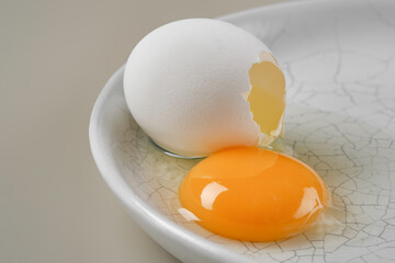 Broken egg with a yellow yolk in a white plate and hole in white egg. Shallow depth of field