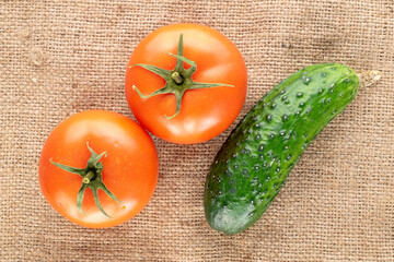 Two organic tomatoes and cucumber on jute fabric, macro, top view.
