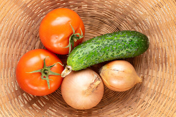 Two organic tomatoes, two onions and a cucumber in a straw bowl, macro, top view.
