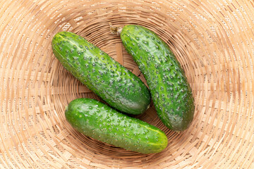 Three ripe cucumbers in a straw bowl, macro, top view.