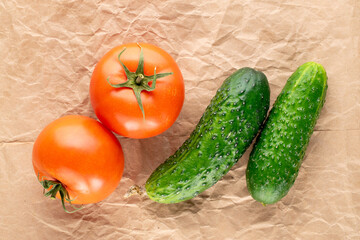 Two organic tomatoes and two cucumbers on craft paper, macro, top view.