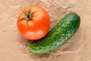 One organic tomato and cucumber on craft paper, macro, top view.