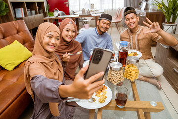 asian muslim friend take selfie together with smartphone while having iftar dinner together